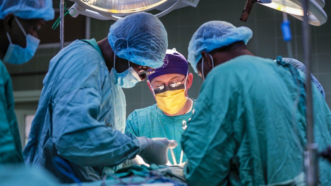 Medical personnel in blue gowns perform surgery at a hospital.