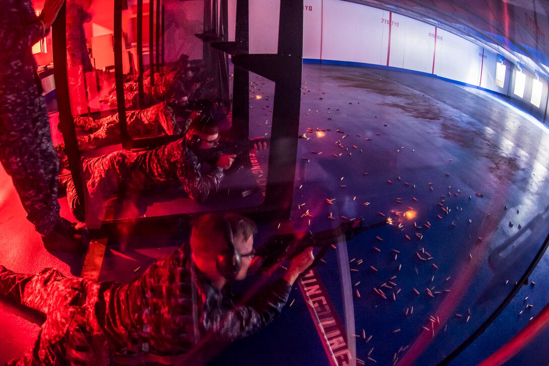Sailors fire M4 carbine rifles under a red light during a weapons qualification.