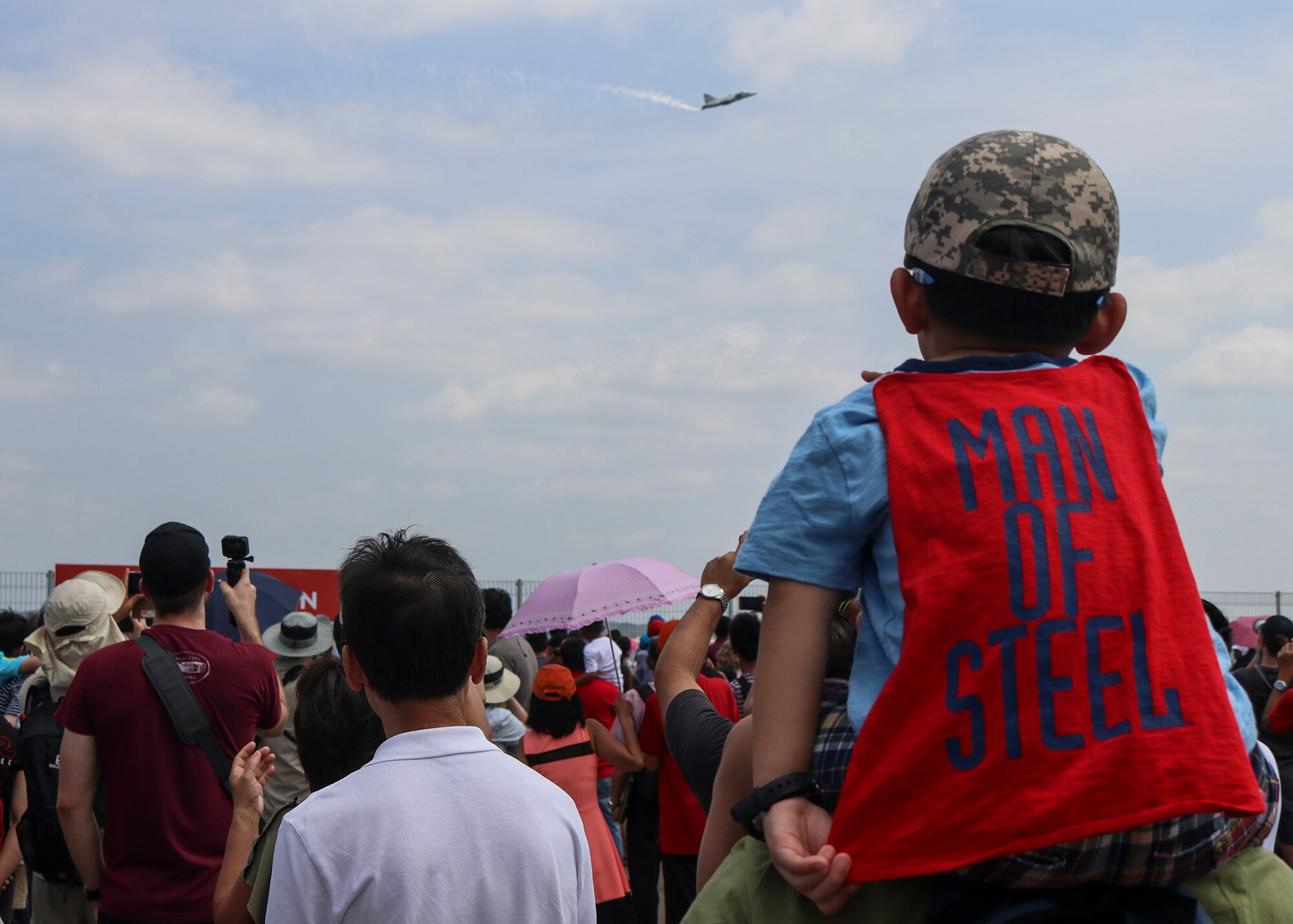 A child sits on his father’s shoulders as a Royal Thai Air Force Saab JAS 39 C/D Gripen performs during an aerial demonstration in the Singapore International Airshow at Changi Exhibition Centre, Singapore, Feb. 10, 2018.