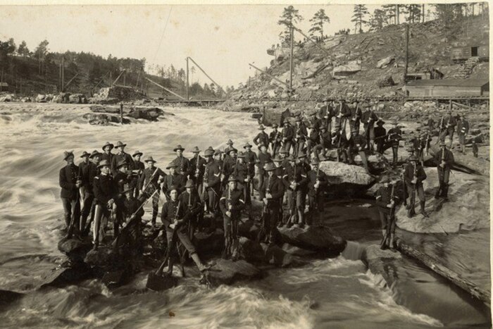 Historical photo of service members standing on stones in a river.