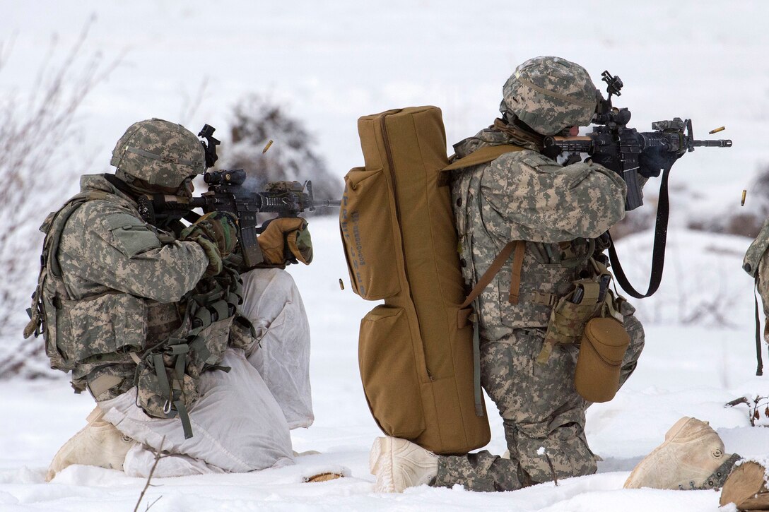 Two soldiers kneel in the snow and fire weapons.