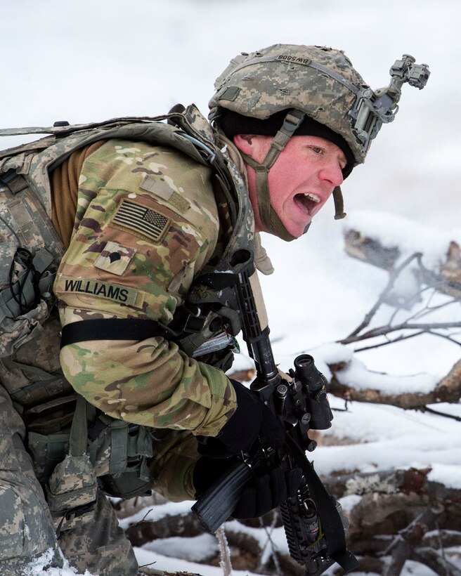 A soldier yells out while crouching in the snow.