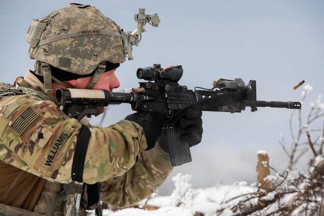 A soldier, shown in profile, fires a weapon the snow.