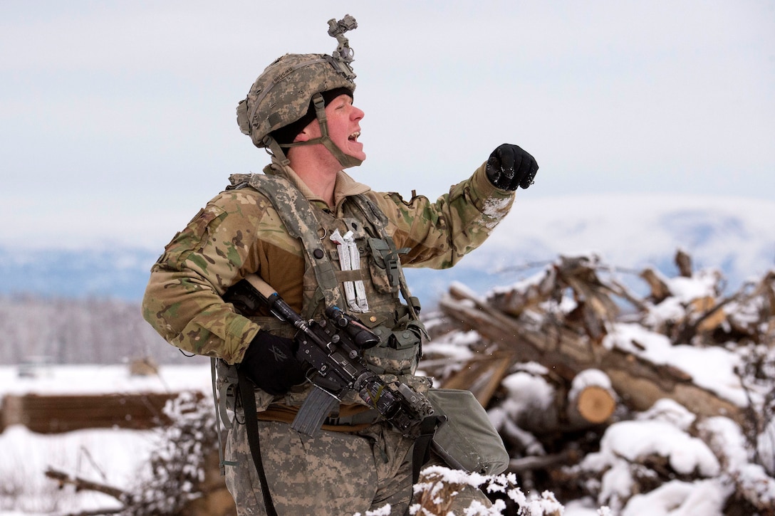 A soldier yells while standing near a log pile in snow.