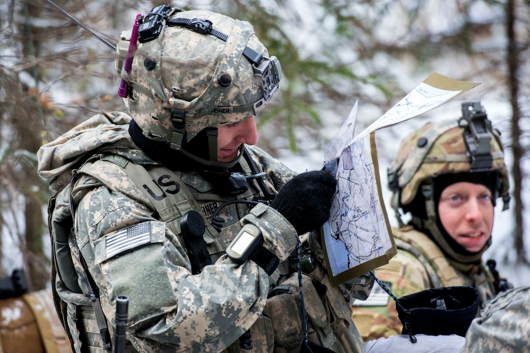 A soldier reads a map as another stands by in the snow.