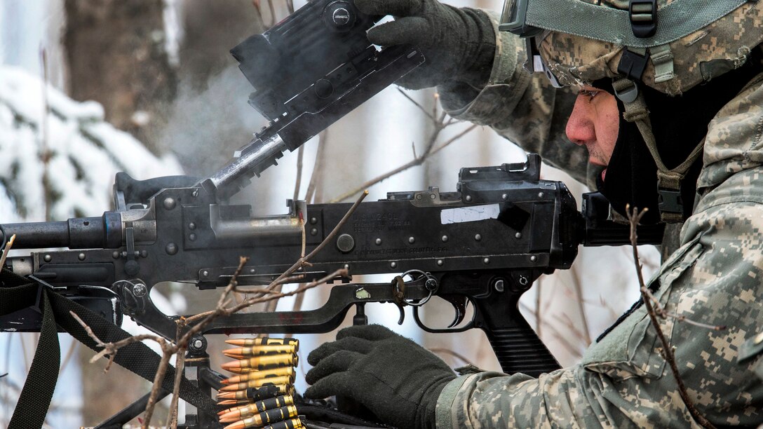 A soldier clears a machine gun while preparing to move during an exercise in the snow.