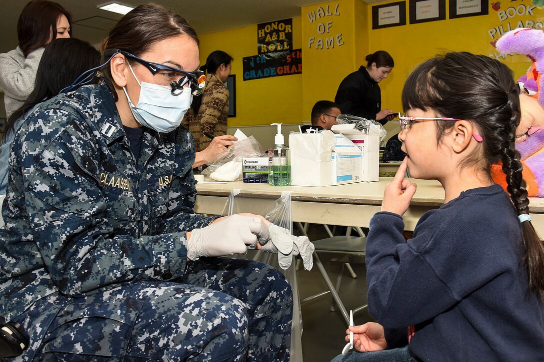 A Navy dentist talks to a student before conducting a dental screening.