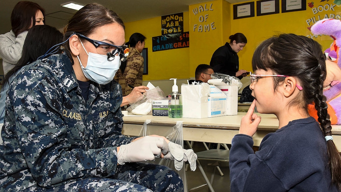 A Navy dentist talks to a student before conducting a dental screening.