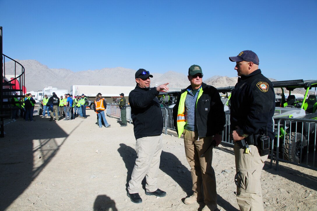 Combat Center Range Safety Officers Gary Santiago, left, and Steve Lomax discuss what's happening with the Can-Am KOH UTV Race with Sgt. Aaron Thiel of the Provost Marshal's Office, Feb. 7, 2018, outside the King of the Hammers operations trailer in Hammertown, Johnson Valley, Calif. Behind them, KOH co-founder Dave Cole leads a tour of Hammertown for members of the media, and volunteer KOH liaison Dawn Rowe talks with law enforcement officers. King of the Hammers is the largest off-road racing and rock-crawling event in North America. (Marine Corps photo by Kelly O'Sullivan)