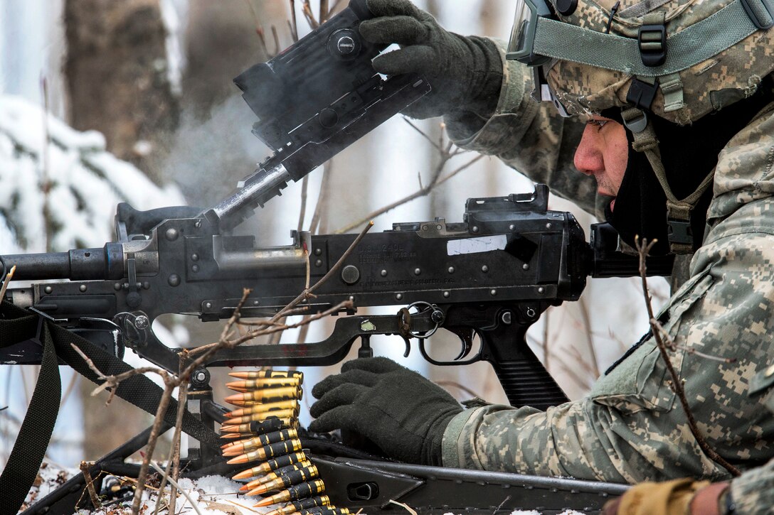 A soldier clears a machine gun while preparing to move during an exercise in the snow.