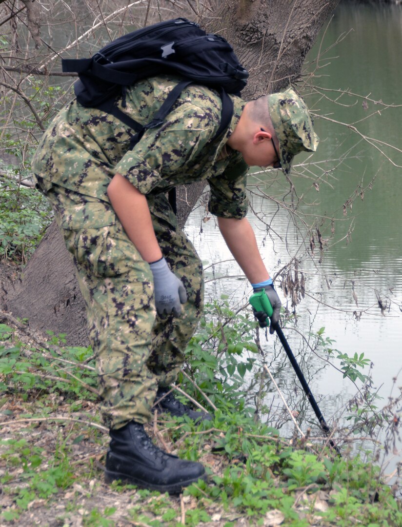 Seaman Ryan Shorter, who is training to become a medical corpsman at the Medical Education and Training Campus at Joint Base San Antonio-Fort Sam Houston, reaches for a piece of trash along Salado Creek during the annual Basura Bash Feb. 17.