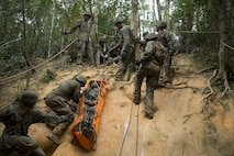 Marines with Communications Company, Headquarters Regiment, 3rd Marine Logistics Group, slide a simulated victim down a hill at the Endurance Course on Camp Gonsalves, Okinawa, Japan, Feb. 16, 2018. The E-Course is the culminating event in the Basic Jungle Skills Course, consisting of obstacles scattered through the hill-riddled jungle. BJSC is designed to teach Marines how to operate in a jungle environment. (U.S. Marine Corps photo by Lance Cpl. Jamin M. Powell)