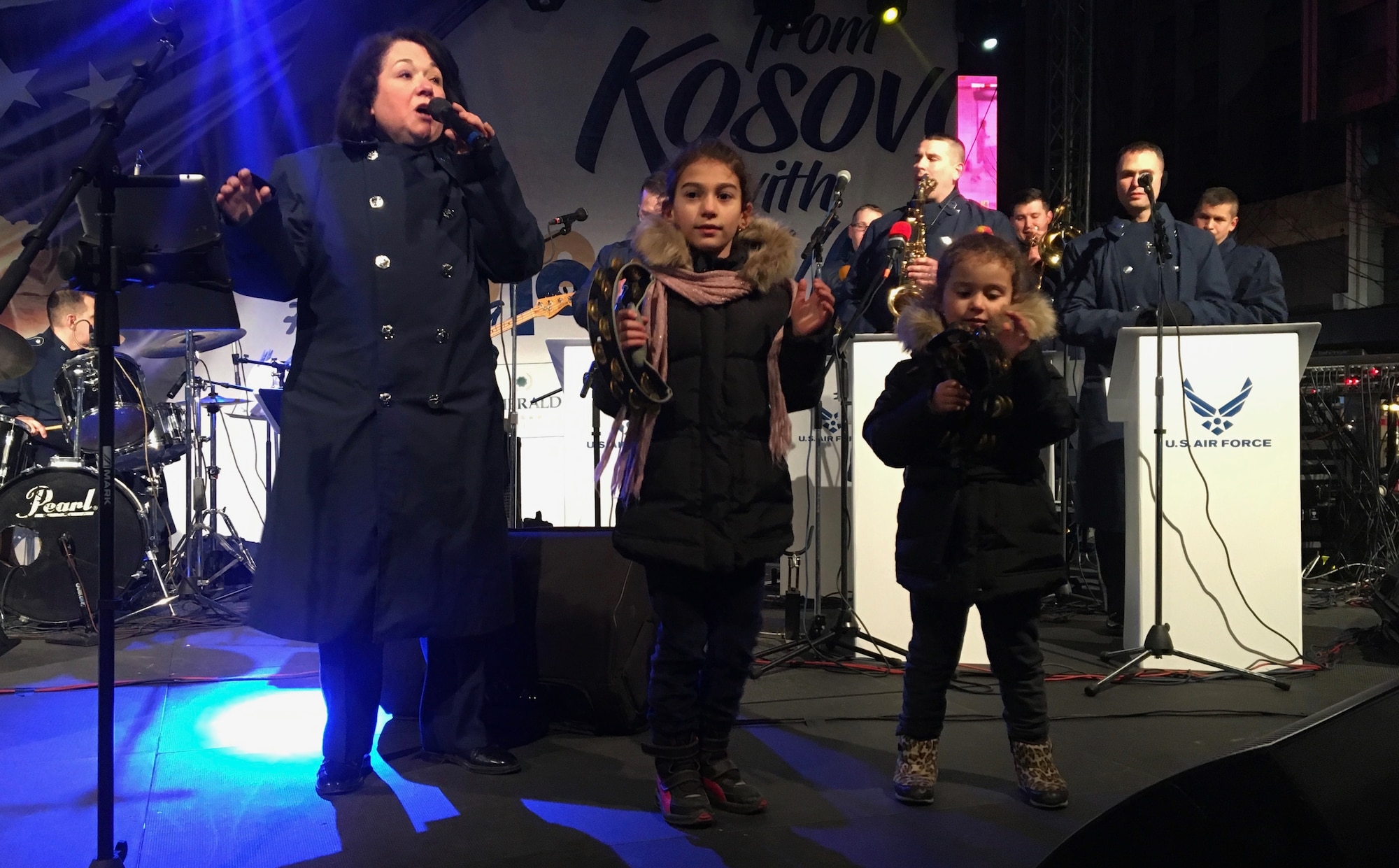 Two local girls join the U.S. Air Forces in Europe Band on stage during a show in Pristina, Kosovo, Feb. 15, 2018. The band visited and performed in Kosovo to celebrate the 10th anniversary of Kosovo independence. (U.S. Air Force photo by Maj. Tristan Hinderliter)