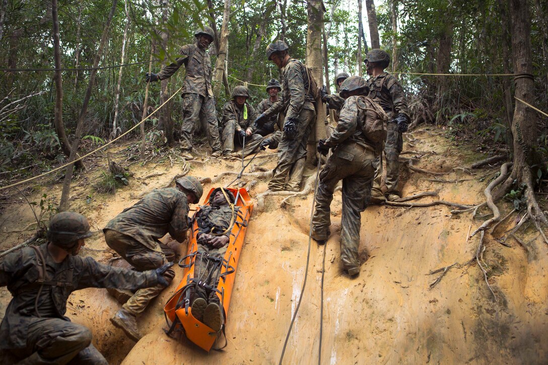 Marines slide a simulated casualty down a muddy hill.