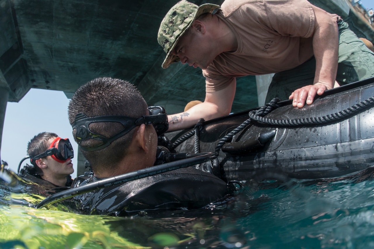 Navy Petty Officer 1st Class Matt Ramirez, a construction mechanic assigned to Underwater Construction Team 2, checks the bottle pressures for Navy Seaman Recruit Adam Porras and a Thai sailor during a dive at Thung Prong Pier in Sattahip, Thailand.