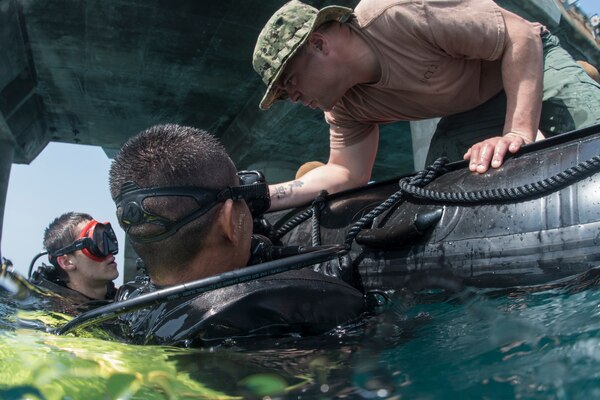 Navy Petty Officer 1st Class Matt Ramirez, a construction mechanic assigned to Underwater Construction Team 2, checks the bottle pressures for Navy Seaman Recruit Adam Porras and a Thai sailor during a dive at Thung Prong Pier in Sattahip, Thailand.