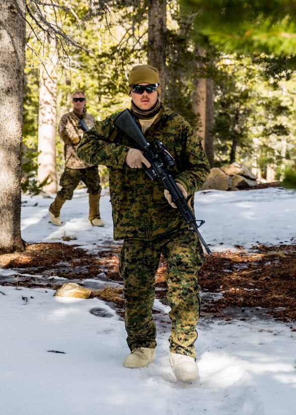 A Marine walks through the snow holding a weapon.
