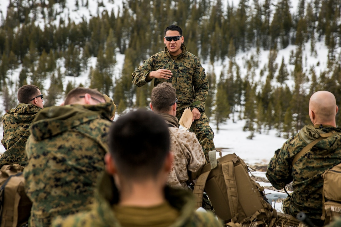 A marines stands while speaking to a group of seated Marines.