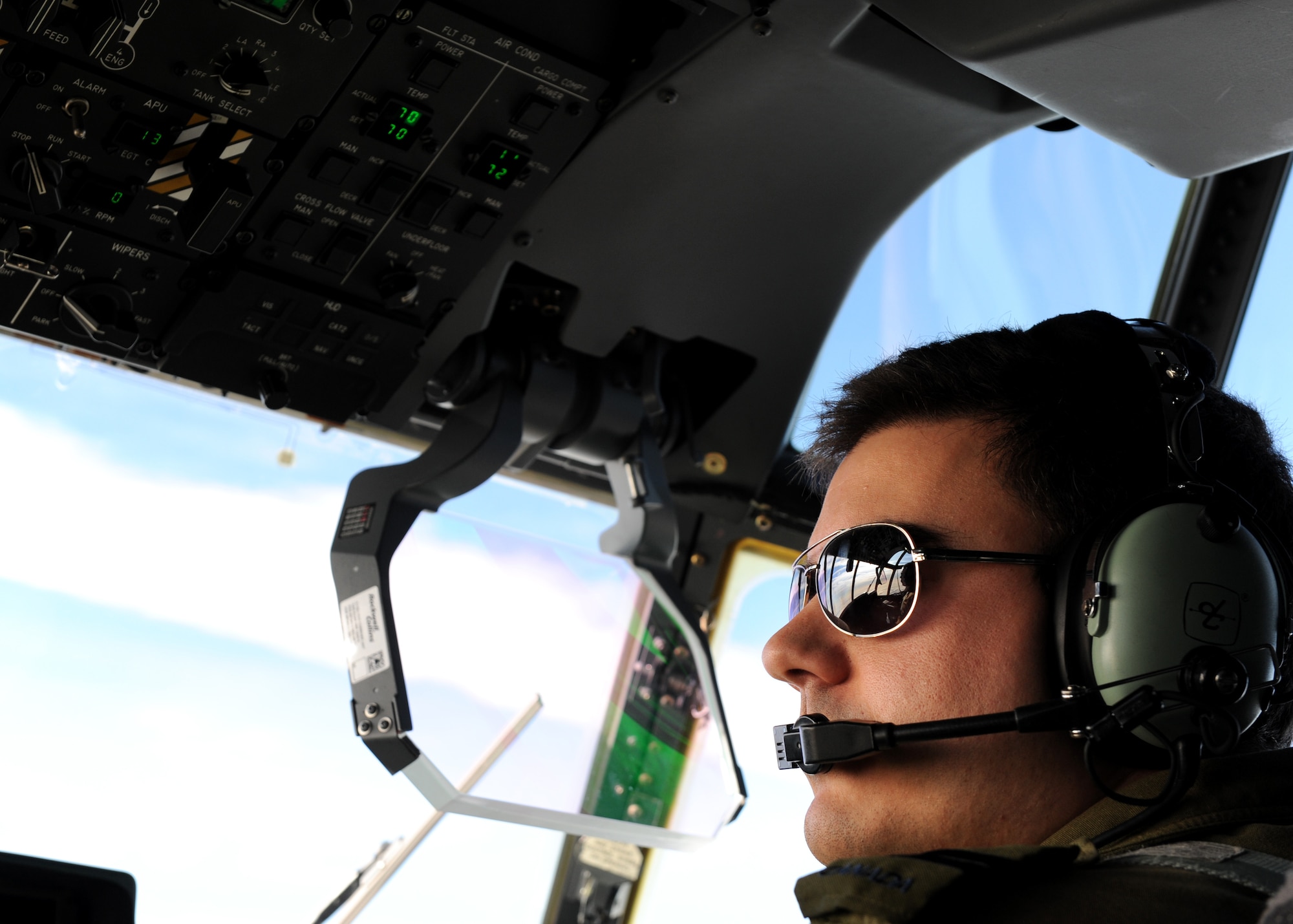 A square photo with a male wearing a headset looking out an aircraft windshield.