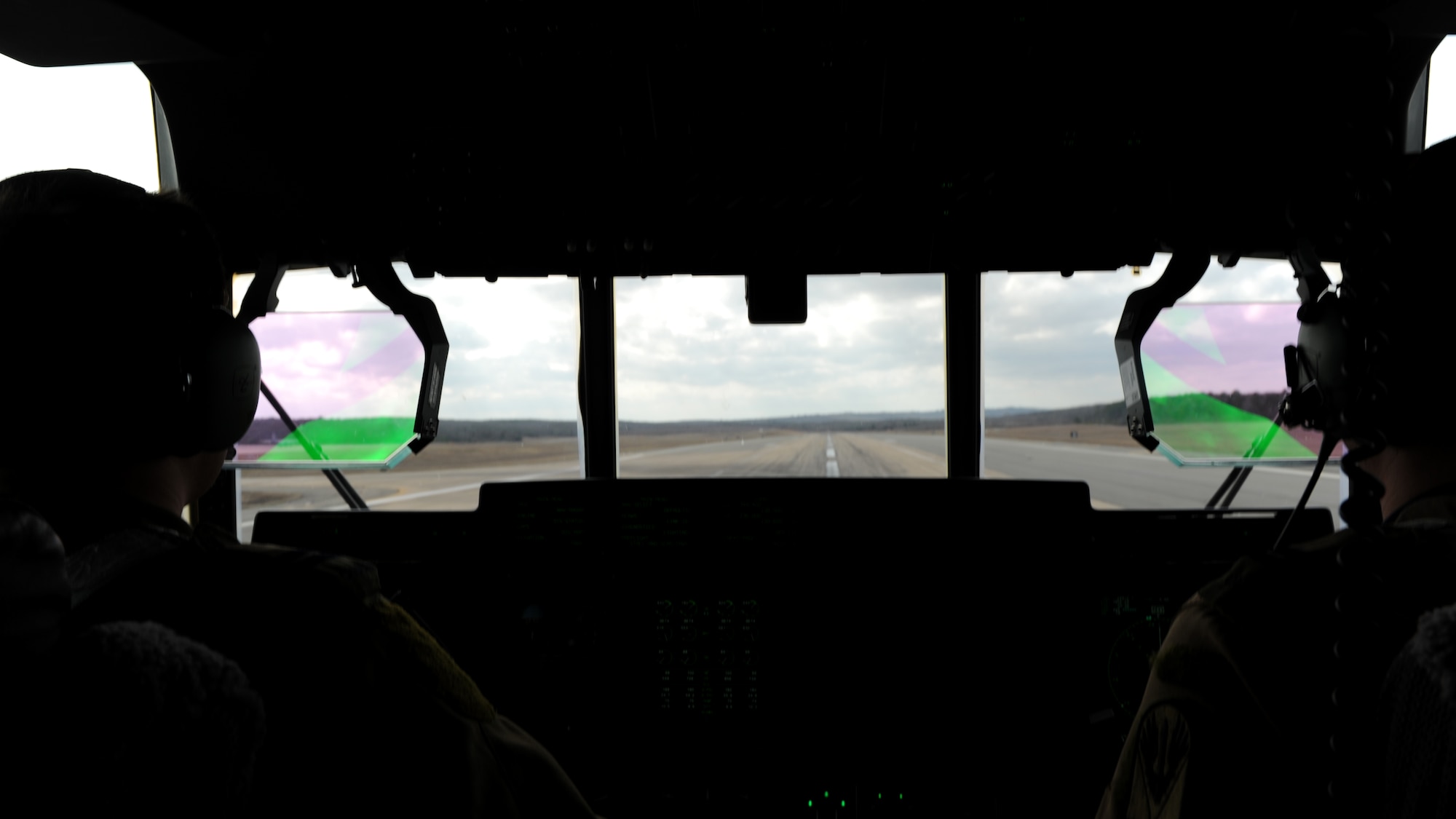 A rectangle photo with two silhouettes in front of an aircraft windshield.