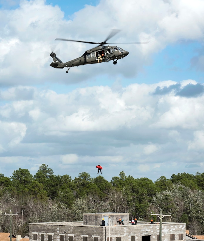 A civilian is lowered from a helicopter to a rooftop to reach a soldier.