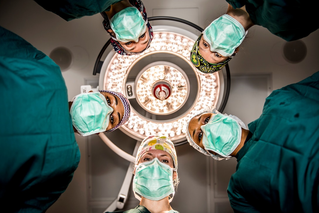 Five felmale surgeons look down at a camera.