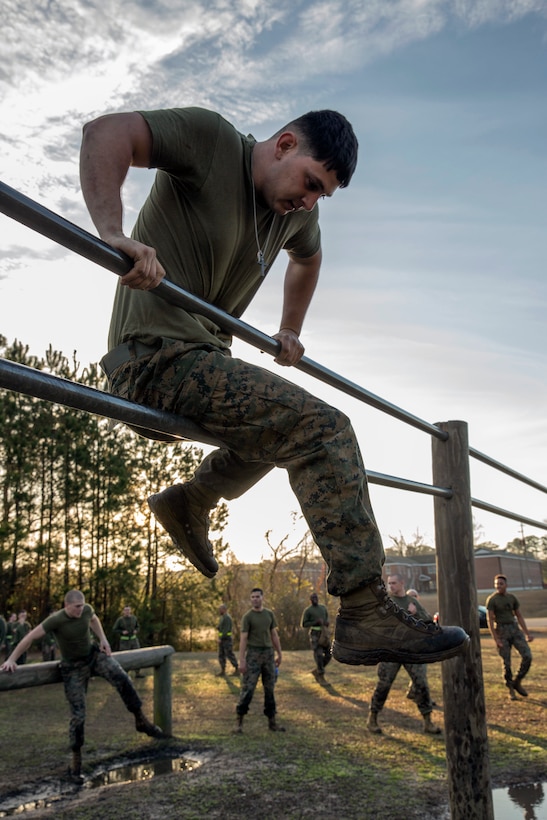 A Marine sits on a metal bar as he tries to climb over a second bar.