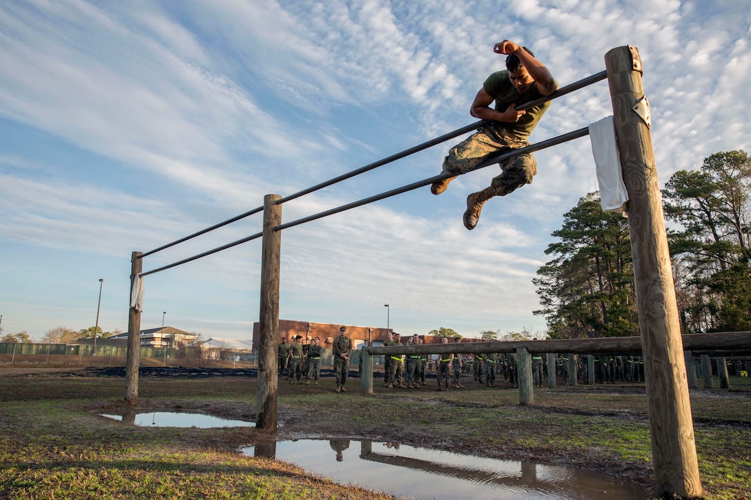 A Marine climbs in between two bars over a water pit.