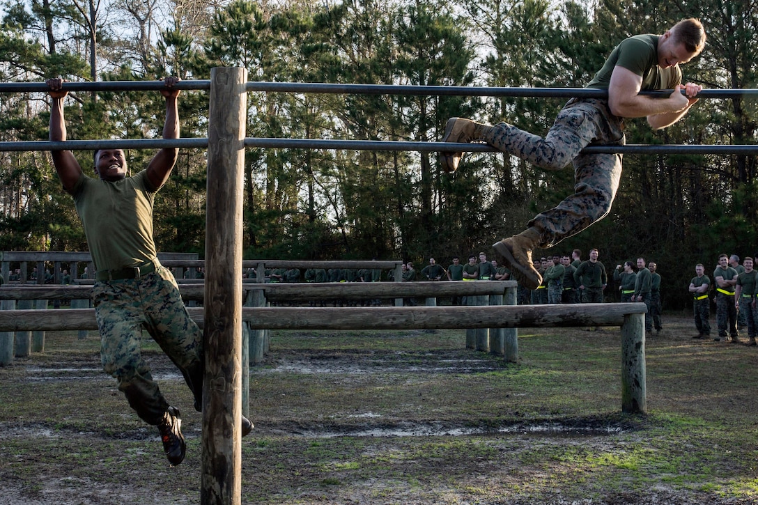 Two Marines climb over metal bars.