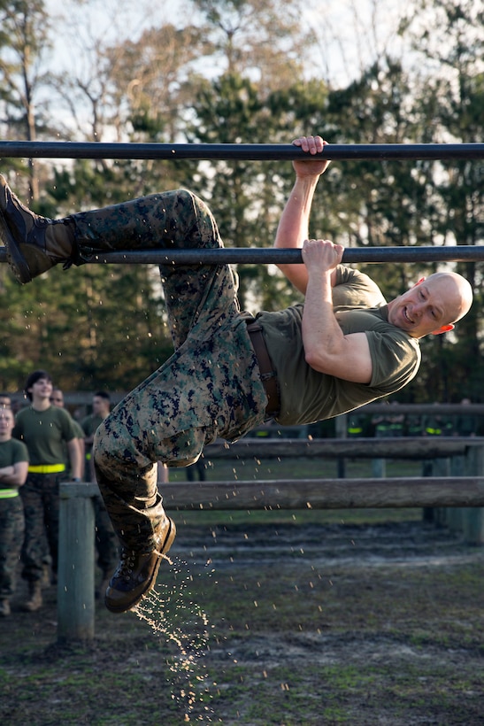 A Marine has a leg wrapped around a metal bar as he pulls himself up.