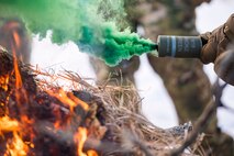 A 91st Missile Security Forces Squadron defender holds a M18 smoke grenade over a signal fire in the Turtle Mountain State Forest, N.D., Feb. 14, 2018. The signal fire’s heat lifts the M18’s green smoke for better signaling. (U.S. Air Force photo by Senior Airman J.T. Armstrong)