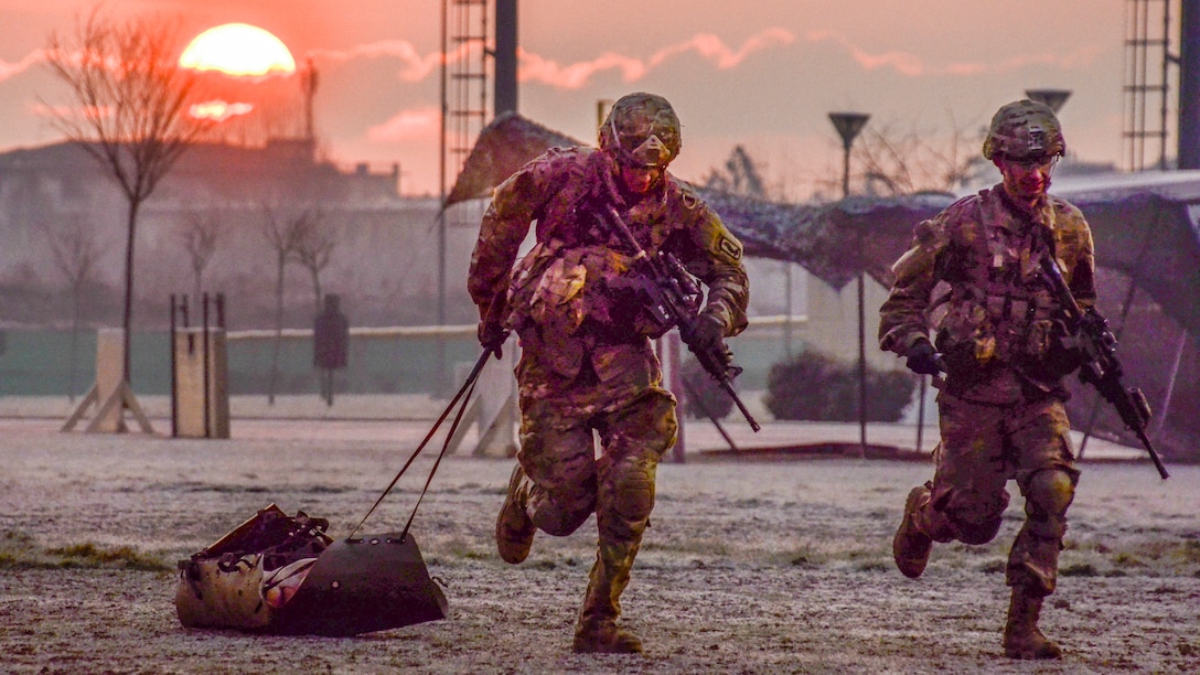 Soldiers run during an event as the sun glows from the horizon