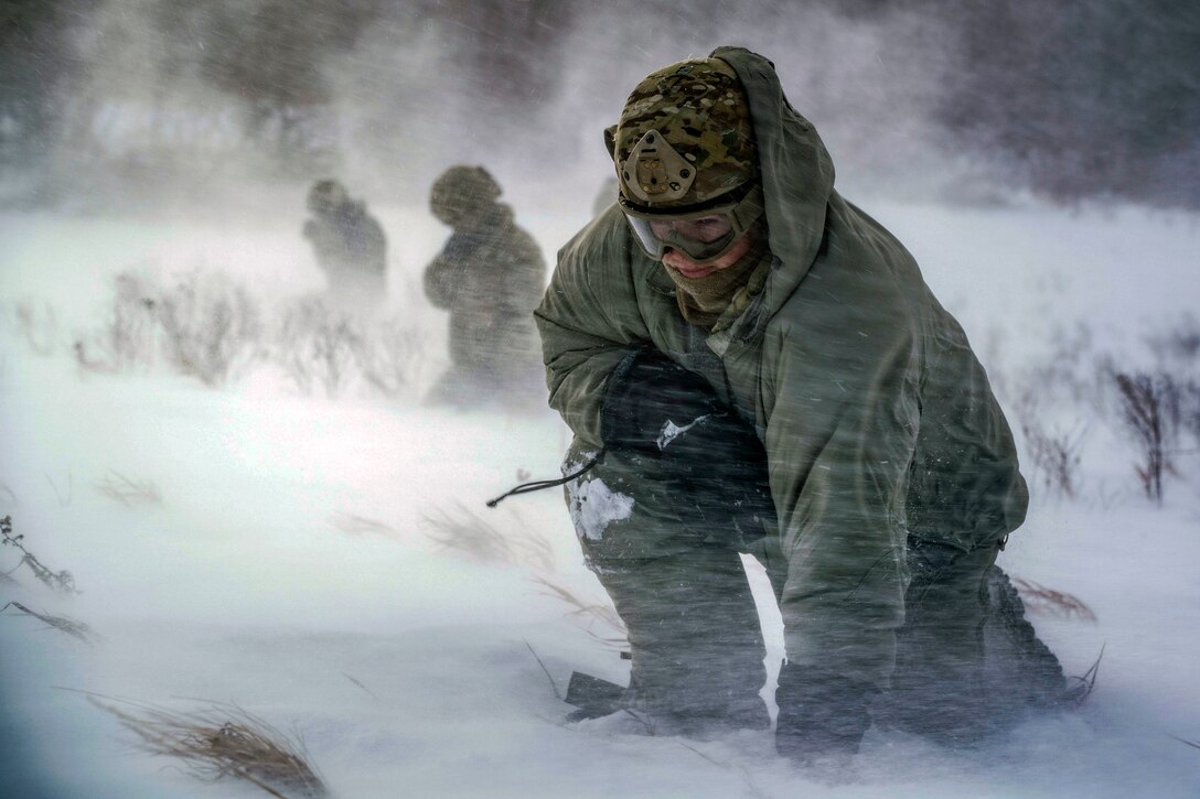 An airman crouches in rotor wash during an exercise.