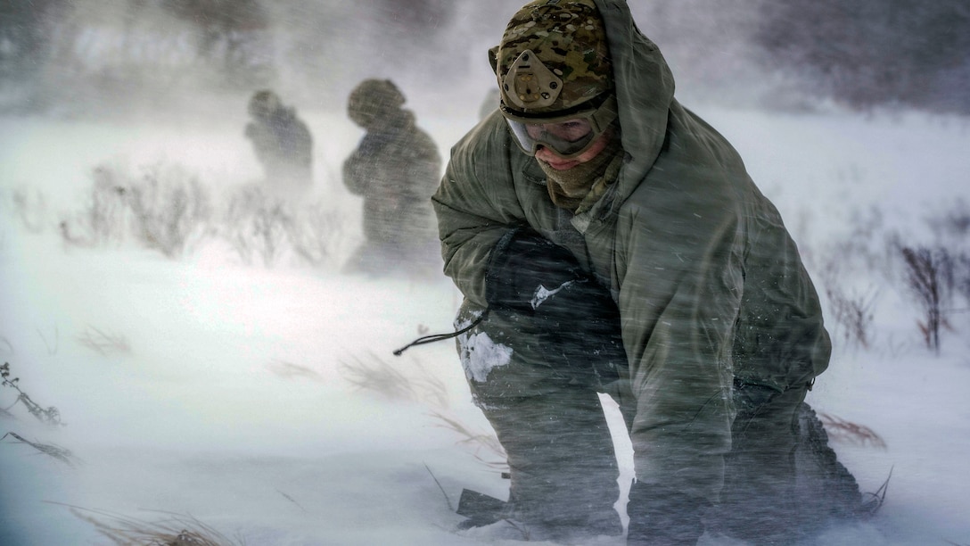 An airman crouches in rotor wash during a field training exercise.