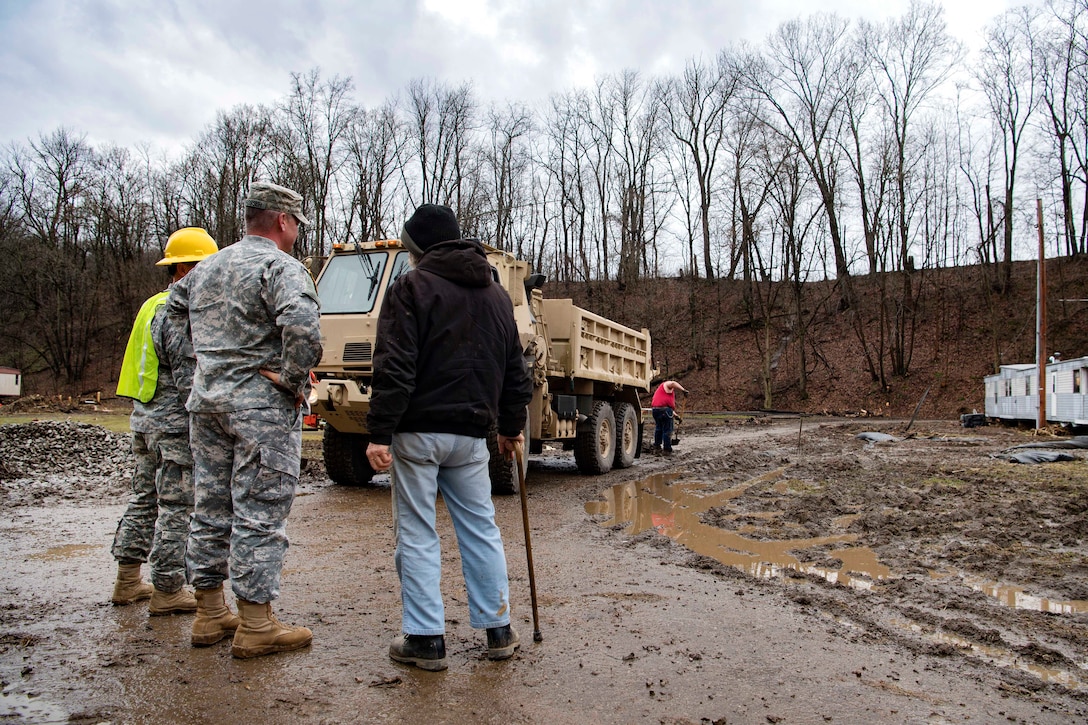Army Chief Warrant Officer 5 Mark Prosser, center, and Staff Sgt. Kevin Smith, left, talk with a local resident during flood recovery efforts.