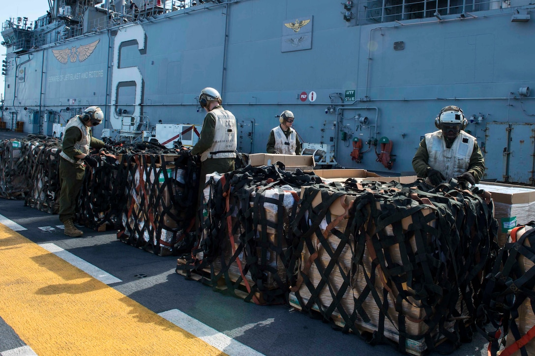 Marines remove cargo nets from supply pallets on a ship.