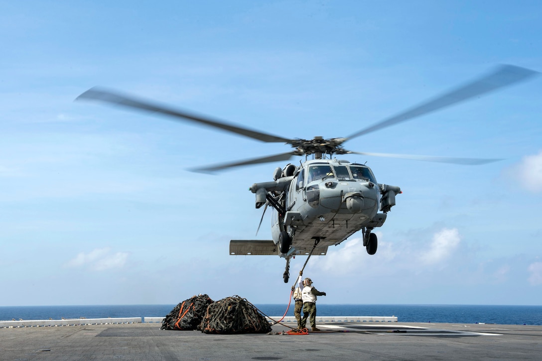 A sailor hooks up cargo nets to an MH-60S Seahawk.