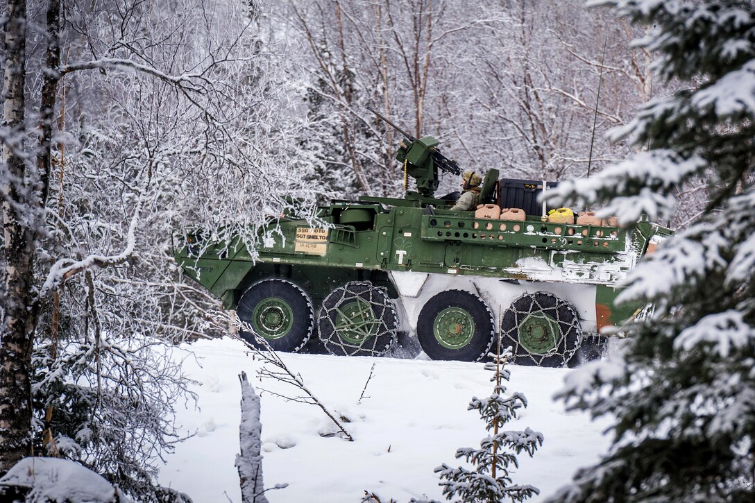 A Stryker armored vehicle is driven through snow in a wooded area.