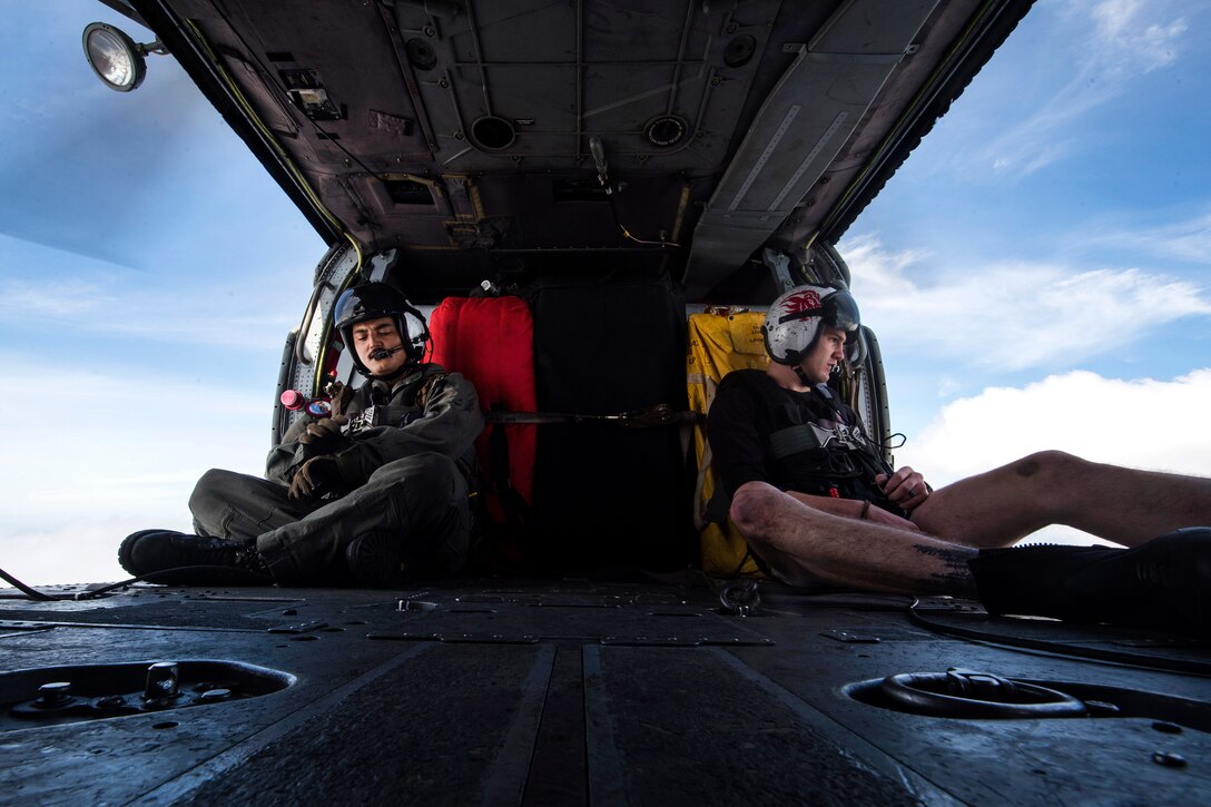 Navy Petty Officers 2nd Class Sebastian Mendieta, left, and Dalton Branson monitor the flight inside an MH-60S Sea Hawk helicopter.