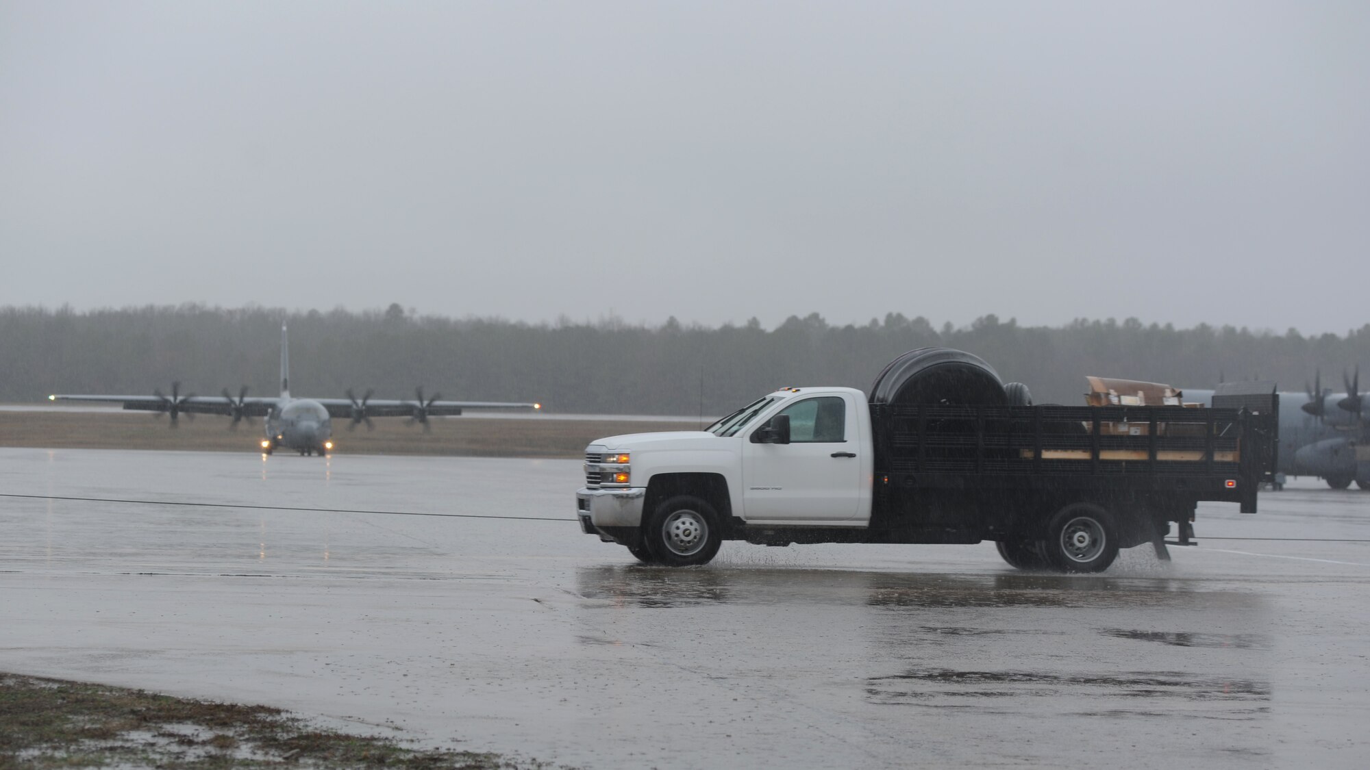 A rectangle photo with a truck on a flightline with an aircraft.