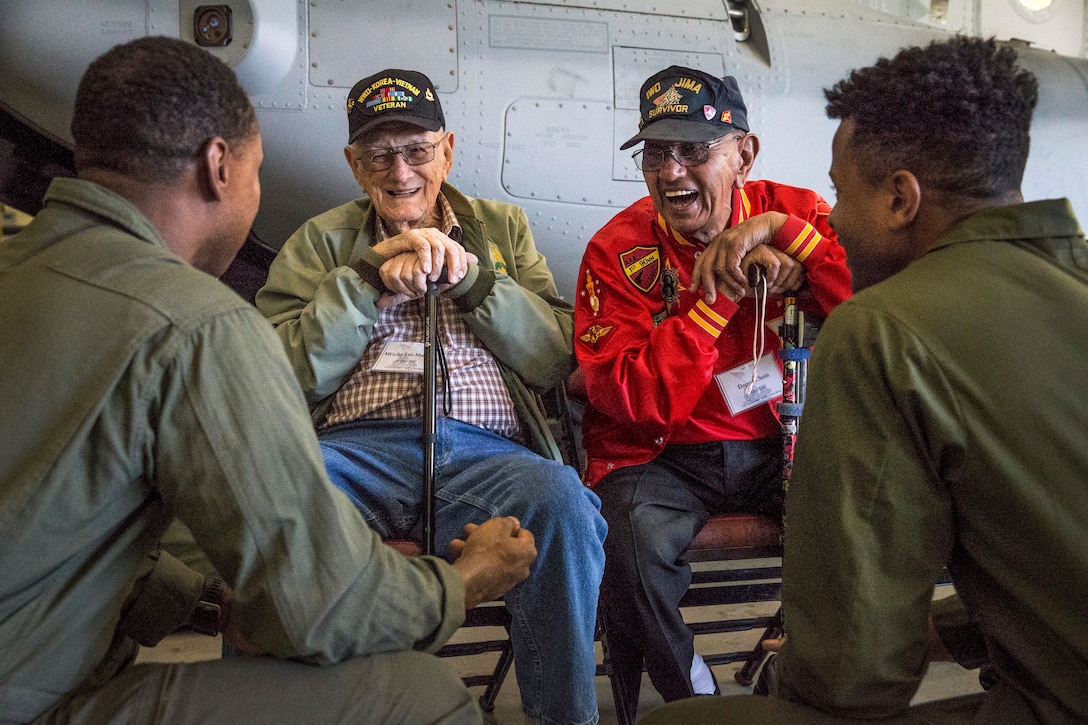 Two veterans lean on canes while sitting and laughing with two Marines.