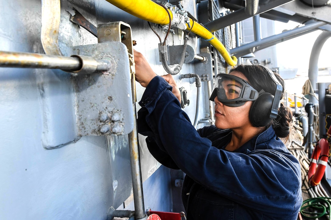 A sailor leans forward scrapping paint.
