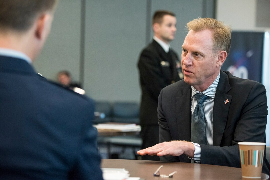 Deputy Defense Secretary Patrick M. Shanahan sits at a table and converses with others.