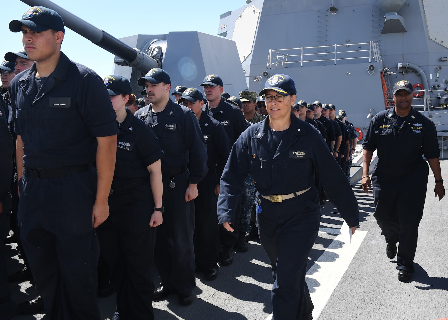 Arleigh Burke-class guided-missile destroyer USS Sterett (DDG 104) Commanding Officer Cmdr. Claudine Caluori, center, and Command Master Chief Monique Greenidge prepare to address the crew during an all-hands call. Sterett is on a scheduled deployment to conduct operations in the Indo-Pacific region. It will also support the Wasp Expeditionary Strike Group (ESG) in order to advance U.S. Pacific Fleet’s Up-Gunned ESG concept and will train with forward-deployed amphibious ships across all mission areas.