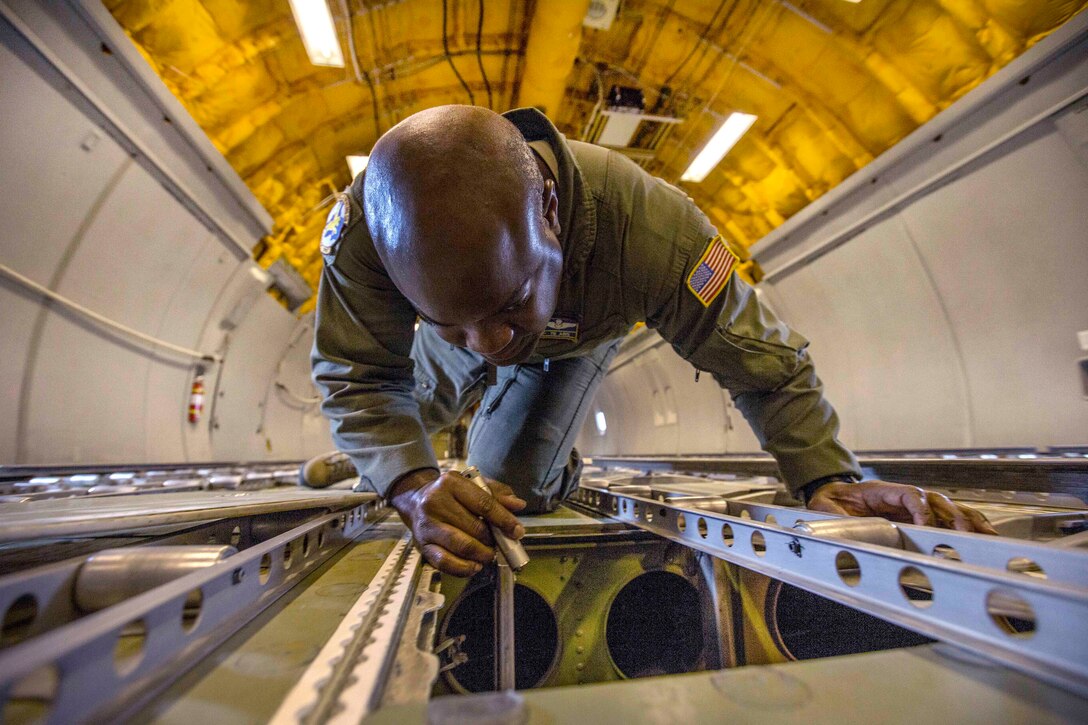 An airman on his hands and knees inspects an aircraft's interior with a flashlight.