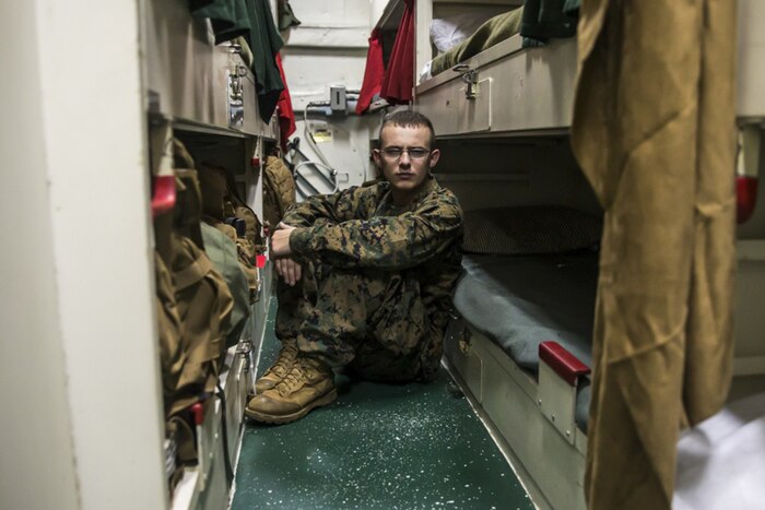 A Marine sits in tight quarters on a ship.