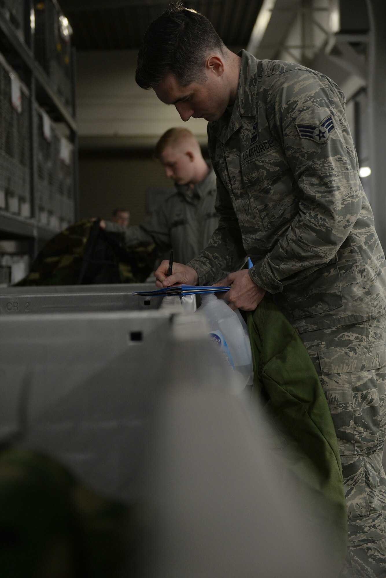 Three Airmen in Air Force Battle Uniforms grab MOPP gear out of bins.