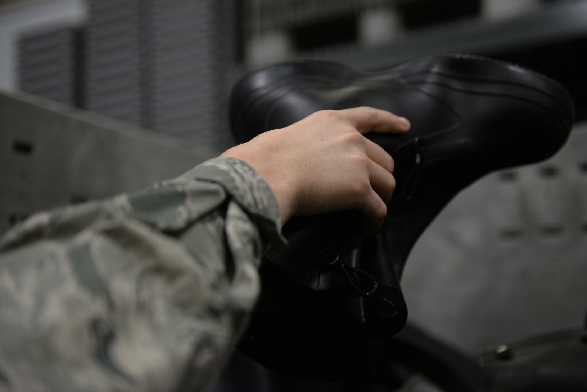 A hand with the Air Force Battle Uniform sleeve picks up a black boot.