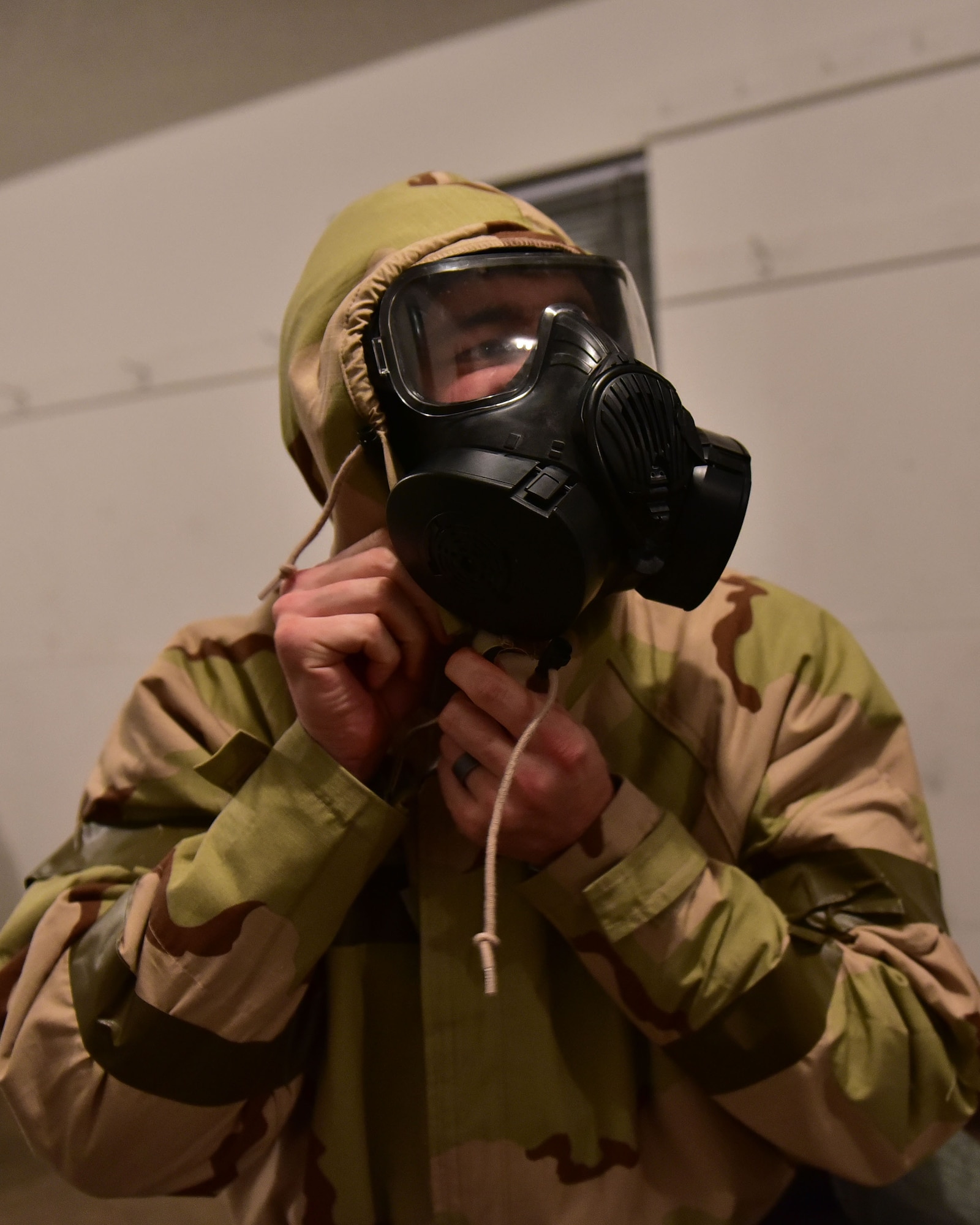 Man fastens hood under gas mask.