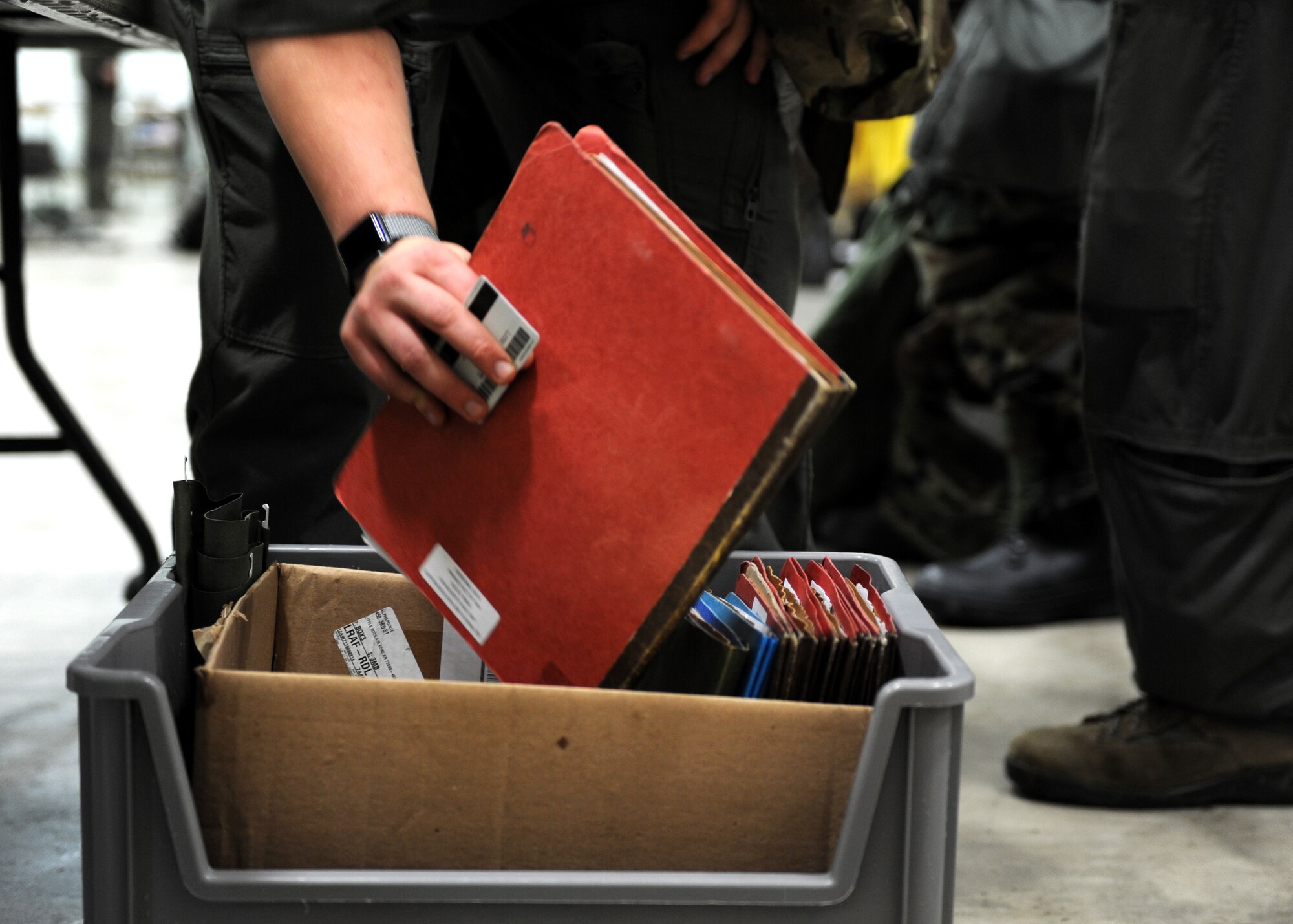A photo with a red folding being placed into a grey container with other folders.